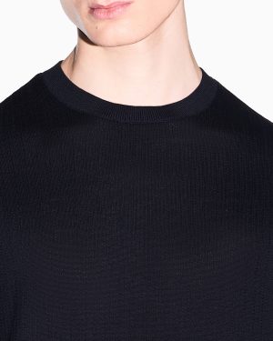 Close-up of a black ribbed crewneck sweater on a person, focusing on the neckline and lower face against a white background.