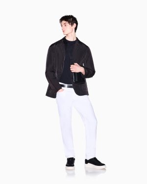 Man wearing a black lightweight jacket over a black shirt, white pants, and a black crossbody bag, looking to the left.