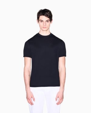 Male model wearing a black crew-neck T-shirt and white pants, standing against a white background.