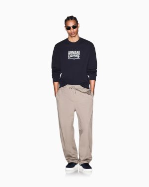 Full-body man wearing a navy Armani Exchange sweatshirt and beige drawstring pants, sunglasses, and black sneakers with white soles.
