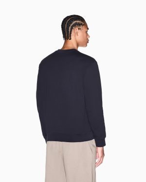 Person viewed from behind wearing a navy sweatshirt and beige pants; hair in cornrow braids in a side profile look to the right